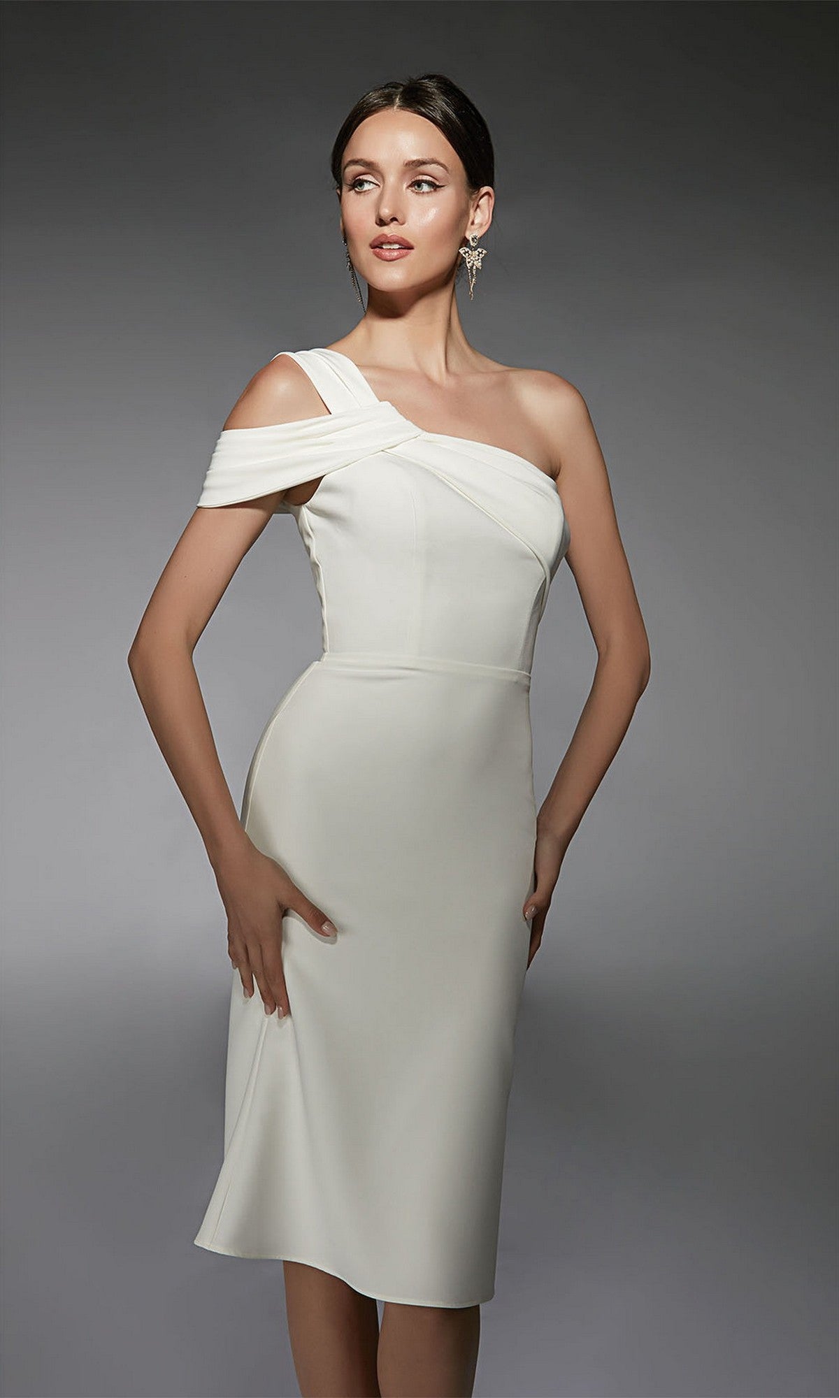 A woman models the Alyce 70054 knee-length semi-formal dress, featuring a fitted silhouette and asymmetrical one-shoulder design, standing against a plain gray background.